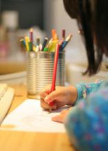 A child uses a colored pencil to write on a sheet of paper.
