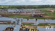 Metal roofs of poultry houses lie on the ground in rows amid twisted metal and debris.