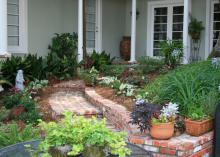 A curving brick walkway lined with plants leads up to a porch.