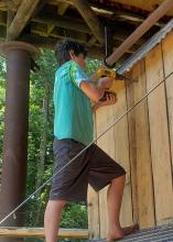 A boy uses a drill to work on a wooden structure.