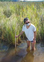 Girl wading knee-deep in water measuring its depth with a yardstick