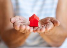 A small red toy house rests in a woman’s open hands.