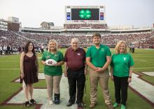 Five people pose for a photo on a football field.