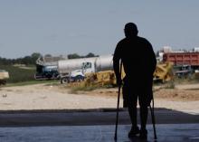 A man stands on crutches in silhouette against a background of farm equipment.