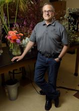 A man stands at a table holding floral arrangements.