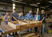A group of people stand in a shop around a woodwork project.