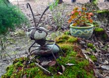 A stone and steel ant sculpture is beside a path through moss.