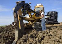 Dylan Yost feeds plastic tubing into equipment that buries drain tile in a deep furrow in fields. This Noxubee County field was being tiled Nov. 8, 2016. (Photo by MSU Extension Service/Kevin Hudson)