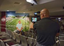 Brian Utley, video producer with MSU Extension’s Agricultural Communications, focuses a camera on former MSU football quarterback Dak Prescott in July 2016. Prescott is the face of the 2017 Public Service Announcement campaign for the 70x2020 Colorectal Cancer Screening Initiative. (Photo by MSU Extension/Kevin Hudson)