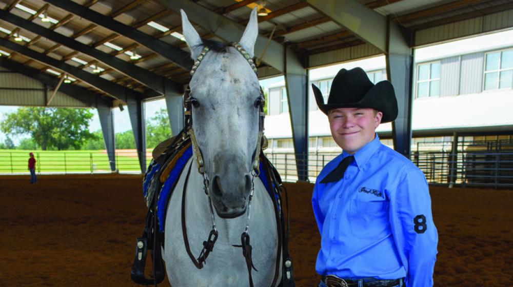 White horse stands beside teen boy with blue dress shirt and black cowboy hat