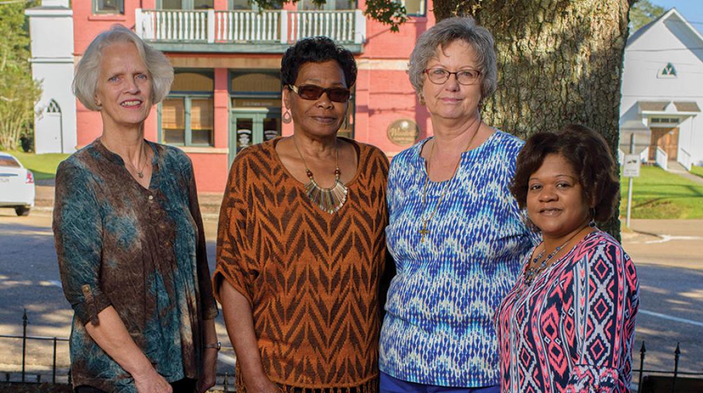 Four women stand next to each other under the shade of a tree.