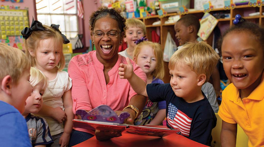 A woman happily reading a book to several small children.