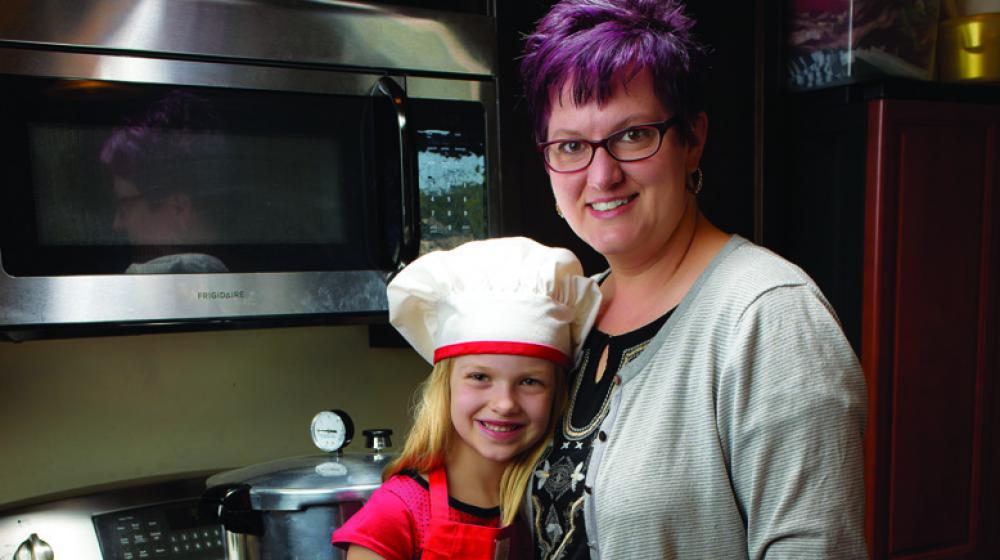 A little girl in a white chef’s hat stands beside her mother