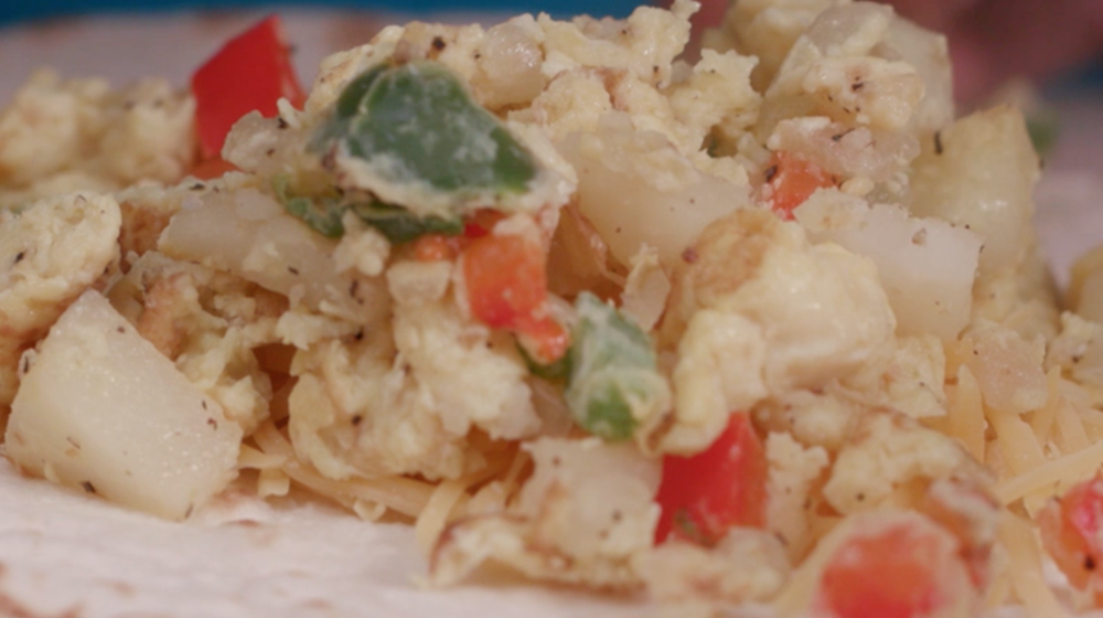 A mixture of diced onions, green and red bell peppers, scrambled eggs, and shredded cheese on a flour tortilla.