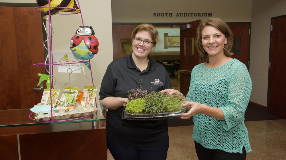 Two women hold a tray of microgreens.