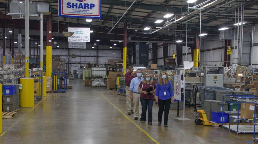 A line of four people walking in a room full of machinery and boxes.