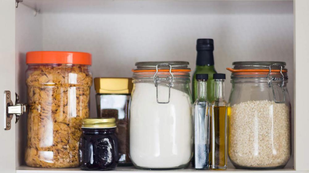 Airtight jars of cereal, rice and flour sit in a cupboard.