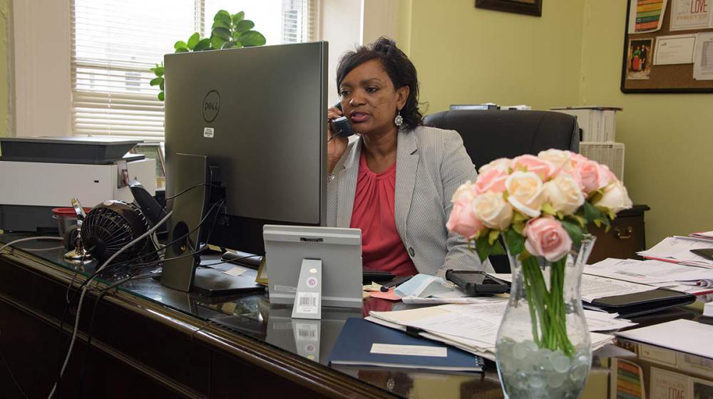 A woman sits behind a desktop computer at a desk talking on the phone.