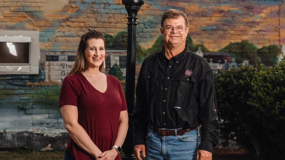 A woman and a man standing in front of a mural and lamppost.