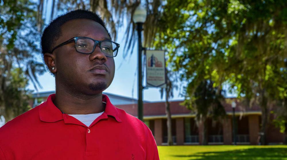 A young man, wearing glasses and a red shirt, standing outside and looking over the horizon.