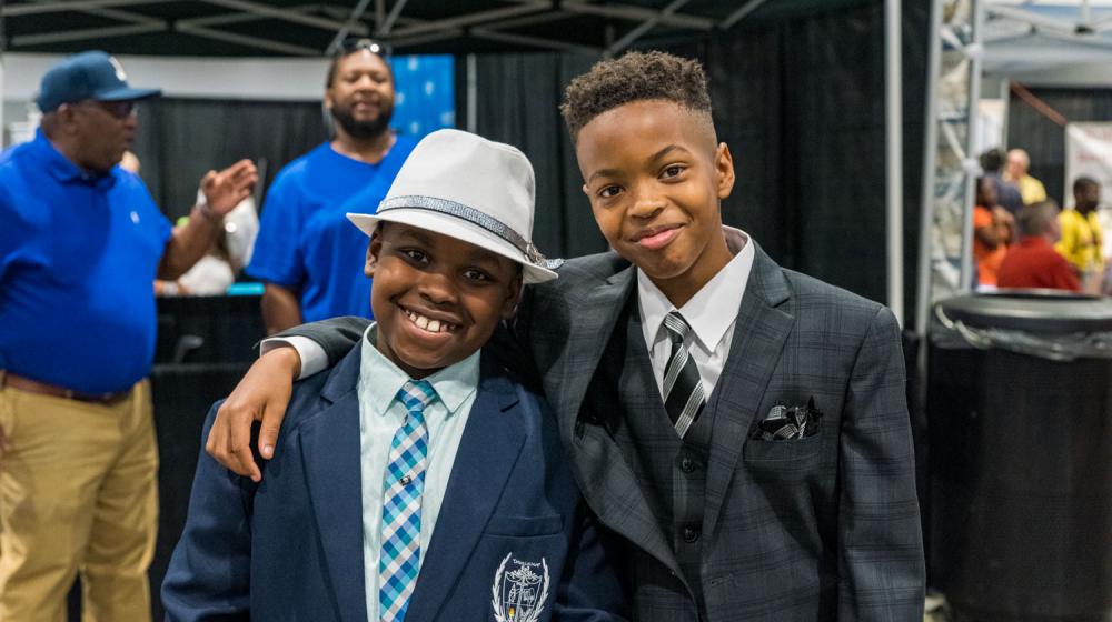 Two boys, wearing suits and fedoras, smiling.