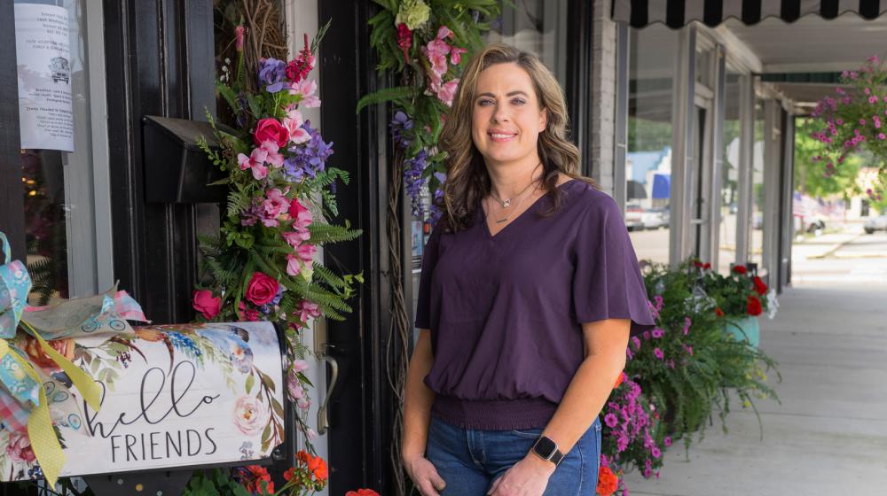 A woman standing outside beside flowers wreathing a door.