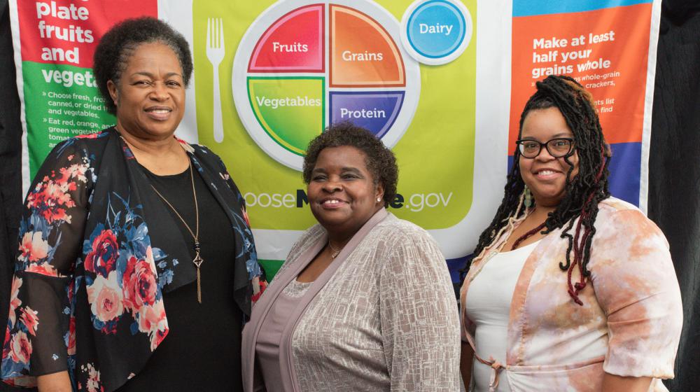 Three women standing in front of a MyPlate banner.