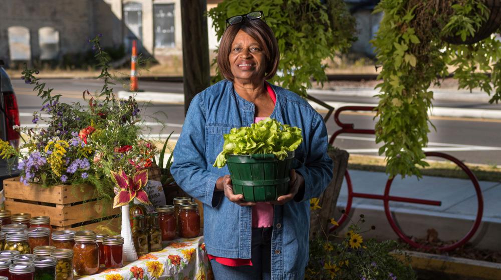 A woman smiling and holding a planter full of lettuce.