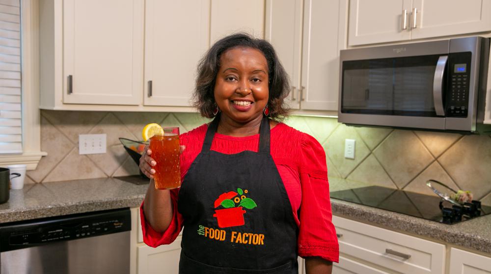A woman holds a glass of strawberry gree tea in a kitchen.