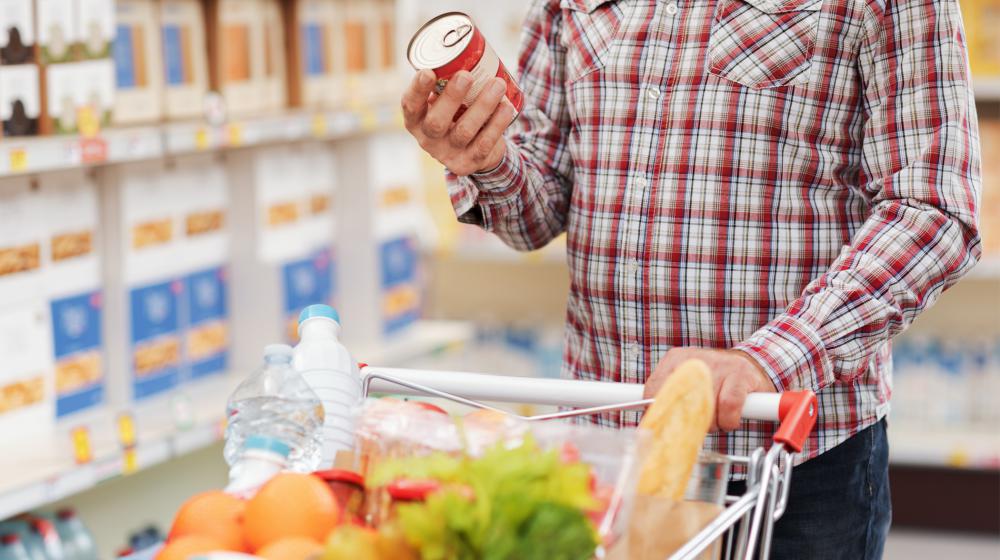 A person reads a Nutrition Facts label on a can of food in the grocery store.