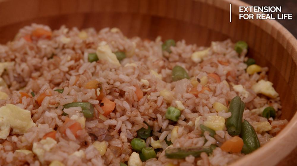 A brown bamboo bowl filled with fried rice made with brown rice, scrambled egg, and mixed vegetables including green beans, peas, carrots and corn. 