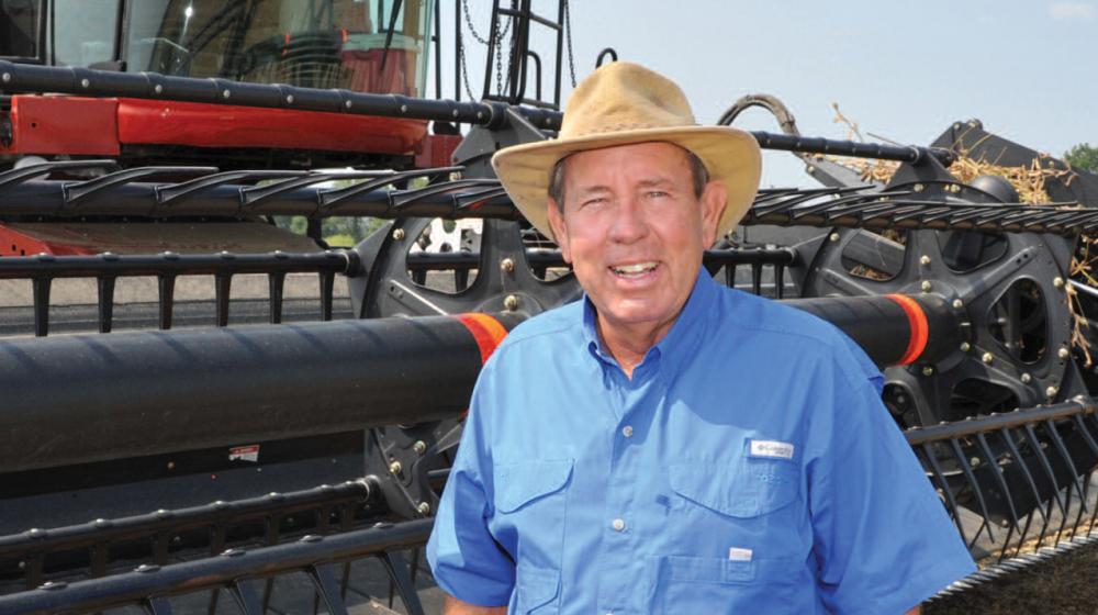 A man wearing a blue shirt and cowboy hat stands in front of a piece of farming machinery.