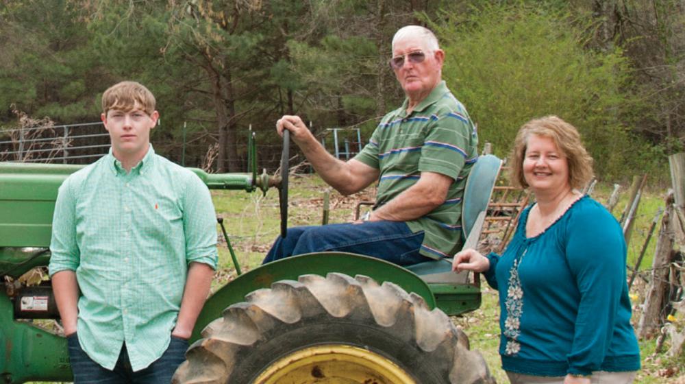 An older man, a woman, and a teenage boy around a green tractor.