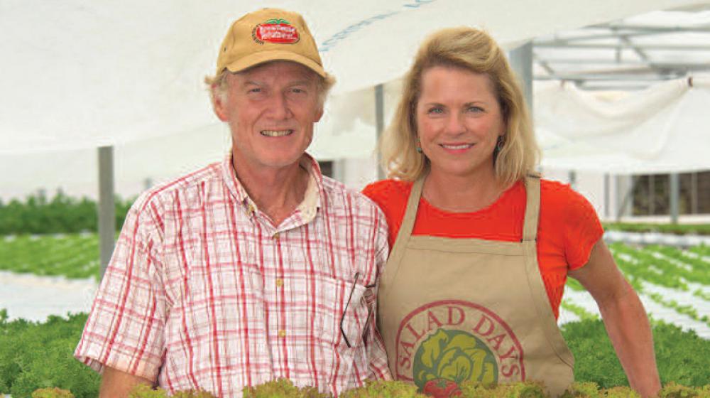 A man and woman behind plants in a greenhouse.