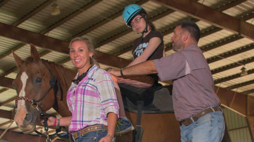 A girl on a brown horse led by a woman and man.