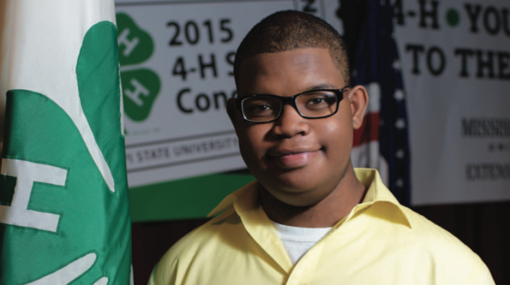 A young boy next to a 4-H flag.