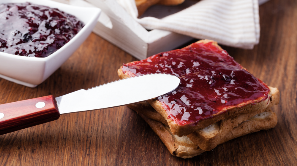 A knife spreading strawberry jam on toast.