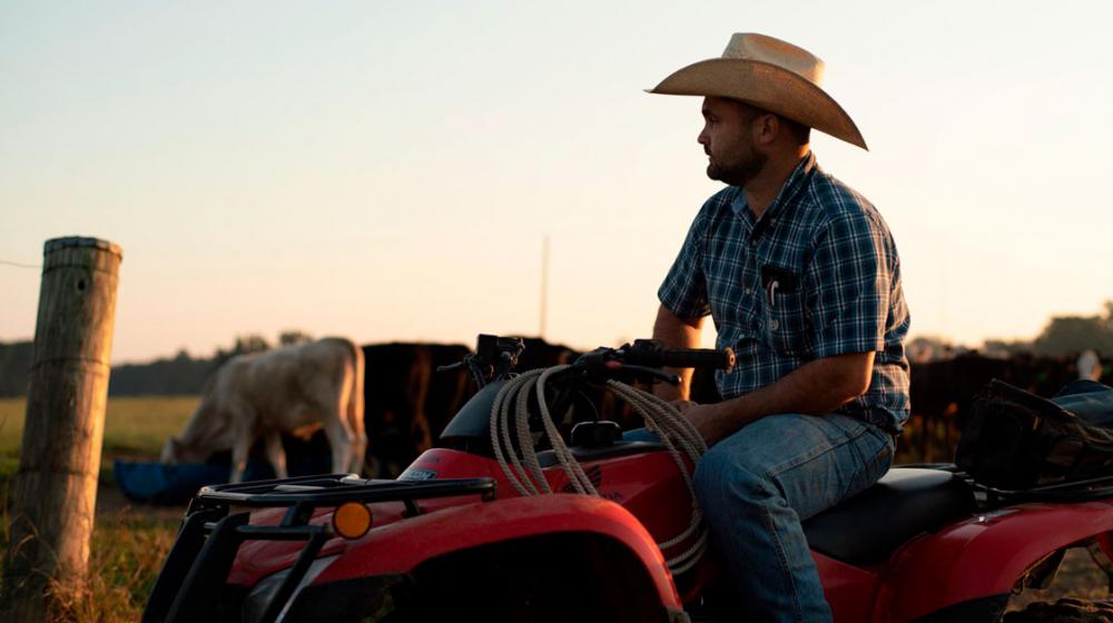 A man wearing a cowboy hat sits on an ATV in front of cows.