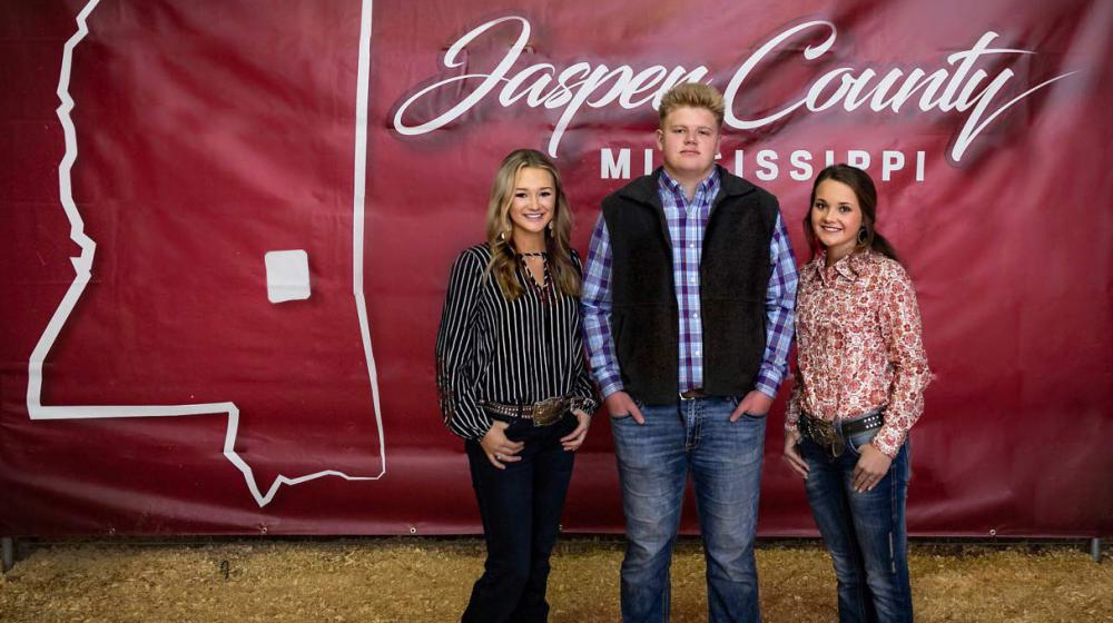 Three young people standing in front of a red banner that says "Jasper County".