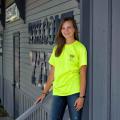 A teen with brown hair and wearing a green Junior Master Wellness Volunteer T-shirt stands in front of the Cleveland, Mississippi, Welcome Center.