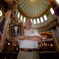 A man with a white 4-H shirt and khaki pants stands in the Mississippi capitol building holding a golden frame with the 4-H green four-leaf clover in the center. Surrounding the logo in a circle are more than 20 4-H pins. 