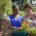 Two women smile as they enjoy colorful potted ornamental plants.