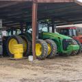 A green tractor, flanked on the right by a smaller red one, stands beneath a metal roof.