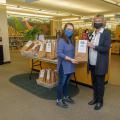 Two masked women with glasses and brown hair holding a brown bag.