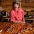 A man with glasses standing behind a table with shells, teeth, and bones on it.