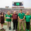 A group of five men and women standing on the MSU football field during a game day. 