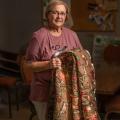 An older woman smiles while holding a quilt.