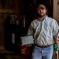 A man stands in a wooden shed holding parts to a soil sensor system.