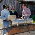 Three men stand around a trailer that holds a large irrigation pipe.