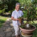 A woman wearing a white shirt with red and blue stars holds a potted plant in a garden.